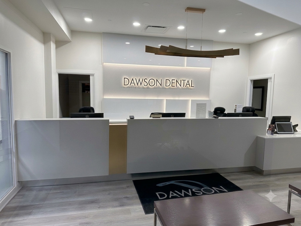 The finished reception — a clean white desk with backlit Dawson Dental signage and warm LED cove lighting, replacing the original dark millwork.