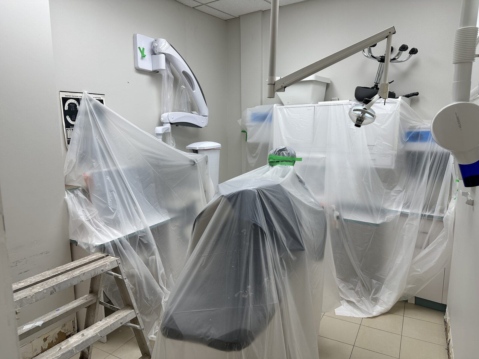 Operatory equipment wrapped in protective plastic sheeting during flooring work.